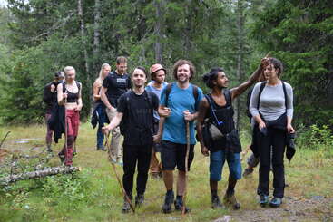 Un groupe de personnes joyeuses se promène dans une forêt verdoyante, sac au dos et bâtons de marche à la main. Ils sourient, profitent de la nature et de la compagnie des autres.