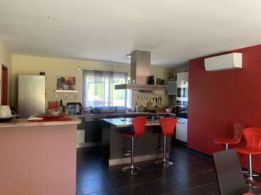This modern kitchen features a center island with red barstools, red accent walls, stainless steel appliances, large window, dark tile flooring, and stylish decor elements throughout.