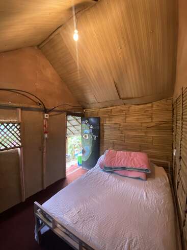 Das Bild zeigt ein gemütliches Zimmer mit einem Einzelbett, Holzwänden und einer Tür, die auf eine Terrasse führt und eine warme und einladende Atmosphäre ausstrahlt.