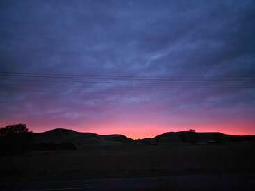 Das Bild zeigt eine ruhige Landschaft mit sanften Hügeln, einem leuchtenden Sonnenuntergang und Stromleitungen, in der Mitte ein dezentes Wasserzeichen mit der Aufschrift \"workaway.info\".