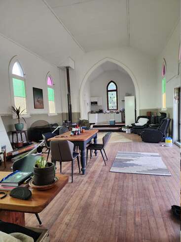 Dieses Bild zeigt eine umgebaute Kirche mit Bogenfenstern mit farbigem Glas, Holzböden, modernen Möbeln, einem Esstisch, einer Küche, Pflanzen und eklektischem Dekor.