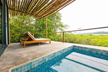 A relaxing modern terrace features a single lounge chair under a bamboo pergola, overlooking lush greenery and a tiled private pool, offering peaceful, scenic tranquility.