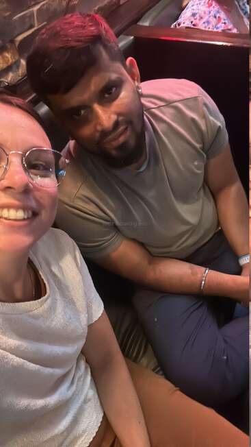 A man and a woman are sitting closely together, smiling for a selfie in a cozy indoor setting, likely a restaurant or cafe booth, enjoying their time.