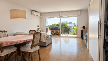 Un salon-salle à manger lumineux et moderne, doté d'un parquet, de grandes baies vitrées, d'un mobilier confortable, d'une table à manger ronde et offrant une vue imprenable sur la verdure.