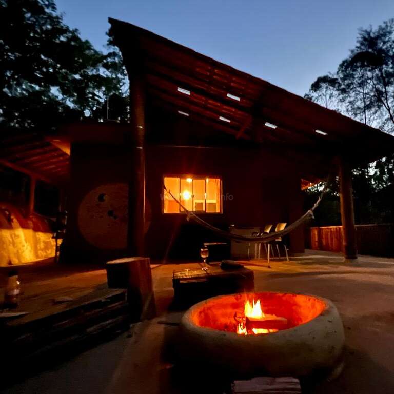 The image depicts a serene outdoor setting at dusk, featuring a fire pit, hammock, and wooden structure, evoking a peaceful and relaxing atmosphere.