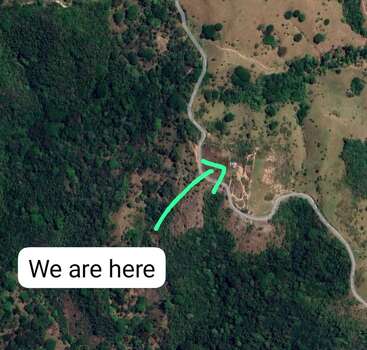 Dieses Bild ist eine Satellitenansicht einer ländlichen Gegend mit kurvenreichen Straßen, dichtem grünen Wald und einem Pfeil, der einen Ort mit der Aufschrift "Wir sind hier" anzeigt.