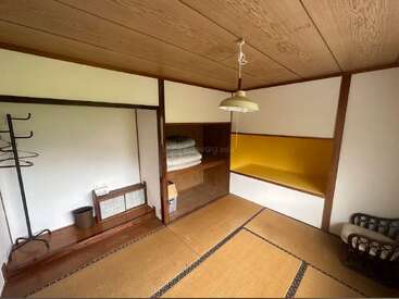 Esta imagen muestra una habitación tradicional japonesa con tatamis, puertas correderas, futones cuidadosamente apilados en un armario, un nicho amarillo y muebles minimalistas de madera.