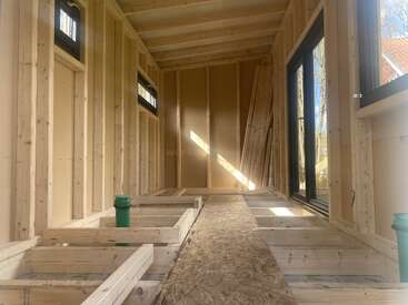 This image shows the interior of a small wooden structure under construction. The framed walls and floor, exposed beams, and large windows allow natural light inside.