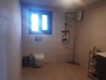 Une salle de bains spacieuse et moderne avec des toilettes murales, une fenêtre, une douche, un chauffe-eau, une poubelle, une étagère et des carreaux de couleur neutre, bien agencés et bien éclairés.