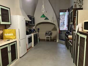 Das ist eine gemütliche, rustikale Küche mit pastellgrünen Schränken, einem weißen Kühlschrank und einem Backofen. Da stehen ein Stuhl, grüne Lampen und ein offenes Fenster.