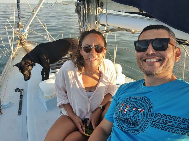 The image shows a man and woman on a boat with a black dog, posing for a selfie with calm water in the background.