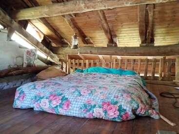 Ein gemütliches Schlafzimmer im Dachgeschoss mit rustikalen Holzbalken verfügt über eine Bodenmatratze, die mit geblümter Bettwäsche bedeckt ist. Natürliches Licht fällt ein und schafft eine warme und einladende Atmosphäre.