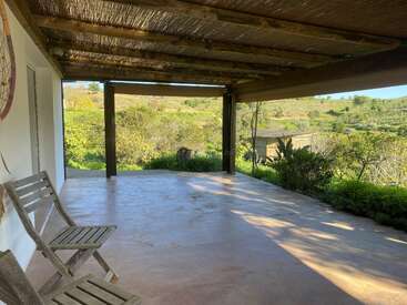 Une terrasse couverte paisible, équipée de chaises en bois, donne sur un paysage verdoyant. Le toit rustique en bois offre de l'ombre, créant ainsi un espace extérieur relaxant et accueillant.