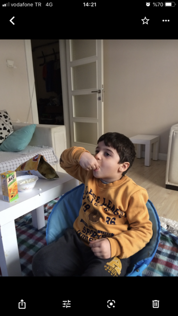 The image shows a young boy sitting in a blue chair, eating popcorn in a living room with a couch and table in the background.