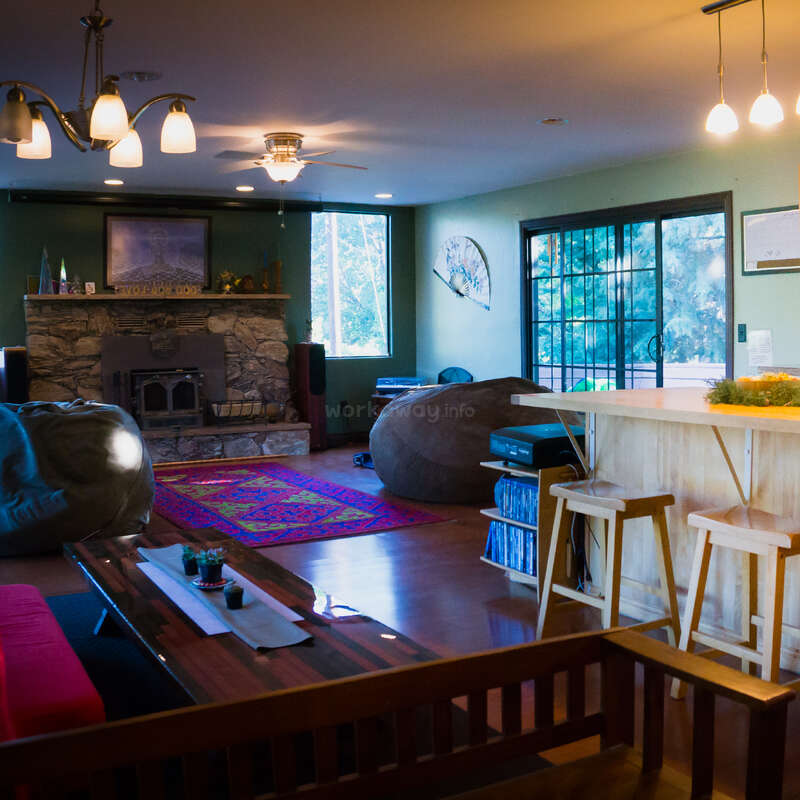 A imagem mostra uma moderna sala de estar em plano aberto com cozinha, sala de jantar e sala de estar, com uma grande ilha e uma lareira, com um esquema de cores neutras e estética minimalista.