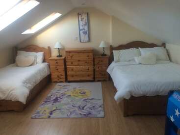 Esta acogedora habitación abuhardillada cuenta con una cama individual, una cama doble, muebles de madera, claraboyas, una alfombra floral, lámparas y un cuadro floral en el techo inclinado.