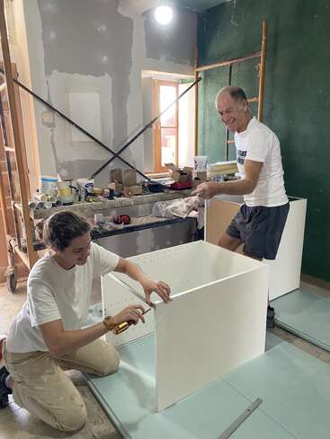 A man and woman assemble a white cabinet together in a room under renovation. They are smiling, surrounded by tools, boxes, and unfinished walls. Construction teamwork.