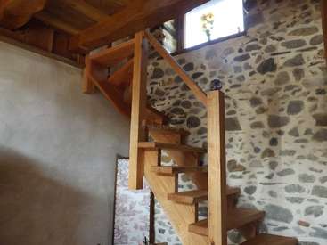 The image depicts a wooden staircase with a stone wall and a window, featuring a vase with flowers on the windowsill.