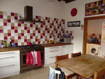The image depicts a kitchen with a brown stove, white cabinets, and a wooden table, featuring a red kettle and various items on the countertops.