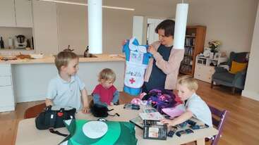 Das Bild zeigt eine Gruppe von Kindern, die draußen spielen. Im Hintergrund sind ein Ball und ein Netz zu sehen, was auf eine lustige und aktive Umgebung im Freien hindeutet.