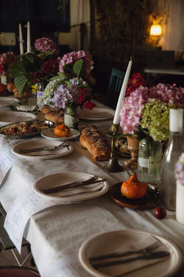 A beautifully set dinner table with floral centerpieces, candles, plates with cutlery, bread, small pumpkins, and a cozy, inviting ambiance for a gathering.