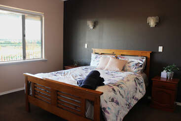 Dieses Bild zeigt ein gemütliches Schlafzimmer mit einem Holzbett, geblümtem Bettzeug, zwei Nachttischen, Wandlampen, einem Fenster mit natürlichem Licht und dekorativen Pflanzen.