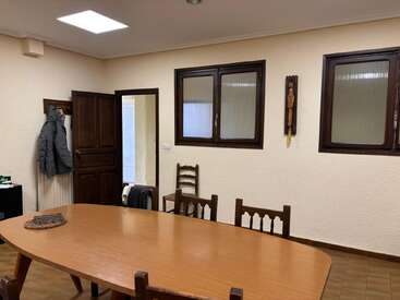 This room has a wooden table with chairs, two windows, a coat hanging on a hook, and a door partly open, revealing another space.