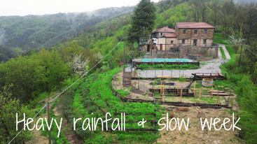 Uma casa de fazenda em uma encosta cercada por uma vegetação verde exuberante após uma chuva forte. Os canteiros e terraços elevados do jardim parecem molhados. O texto sobreposto diz: "Chuva forte e semana lenta".