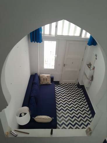 Esta imagen muestra un salón pequeño y acogedor con un sofá azul, baldosas estampadas en zigzag, paredes blancas, cortinas azules y una entrada arqueada vista desde arriba.