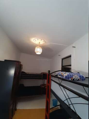 This is a small, well-lit room featuring two metal bunk beds, a wardrobe, a window, pillow with cartoon prints, and a decorative ceiling light fixture.