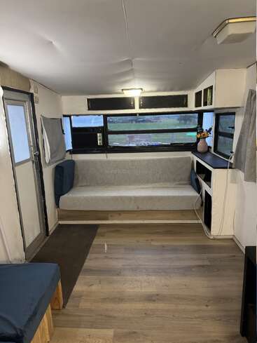 Cette image montre un intérieur de camping-car confortable avec un plancher en bois, un long canapé gris, des placards de pavillon, de grandes fenêtres et une petite table décorée de fleurs.