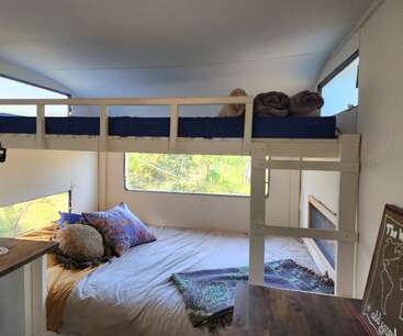 Este acogedor espacio cuenta con una litera sobre una cama grande, almohadas de colores, mantas enrolladas y grandes ventanales que ofrecen vistas de la exuberante vegetación exterior.