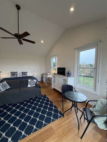 This cozy bedroom features a large bed, dark blue accent pillows, a patterned rug, a ceiling fan, white furniture, and a small table with chairs.