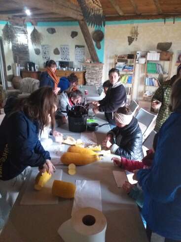 L'image représente un groupe de personnes réunies autour d'une table, occupées à un projet d'artisanat, avec un seau étiqueté "travail" et divers matériaux éparpillés sur la table.