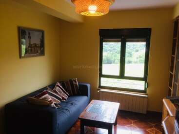 Ce salon confortable comprend un canapé bleu foncé avec des coussins rayés, une table basse en bois, une grande fenêtre offrant une vue panoramique et une lampe suspendue.