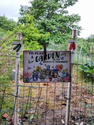 A colorful garden sign reads, "To plant a garden is to believe in tomorrow," surrounded by flowers, seed packets, and greenery, inspiring hope and growth.