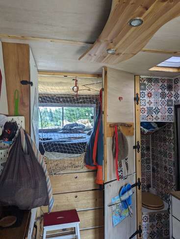 Cette photo montre l'intérieur chaleureux d'un camping-car, avec un lit, des rangements, des paniers suspendus, des touches de bois et une salle de bains compacte aux carreaux à motifs.