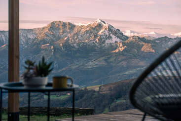 L'image représente une scène sereine d'une chaîne de montagnes avec une petite étendue d'eau, avec un arbre proéminent au premier plan et un ciel clair, évoquant un sentiment de tranquillité.