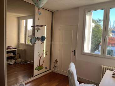 Cette chambre chaleureuse et baignée de soleil est dotée de grandes fenêtres, d'une armoire à miroirs, de stickers muraux ludiques, d'un mobile en forme de montgolfière et d'un parquet. Une chaise et un bureau viennent compléter l'ensemble.