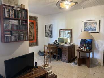 Esta acogedora habitación cuenta con un escritorio abarrotado, una silla de madera y un televisor. En las estanterías hay DVD y CD. Las obras de arte, el tapiz y una gran lámpara le dan un toque especial.