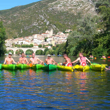 The image depicts a group of people in kayaks on a river, with a bridge and town in the background, set against a mountainous landscape.