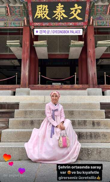Eine Frau in einem traditionellen rosa Hanbok sitzt auf den Stufen des Gyeongbok-Palastes und lächelt. Verschnörkelte Architektur und koreanische Schilder sind über ihr zu sehen. Eine bunte, lebendige Szene.