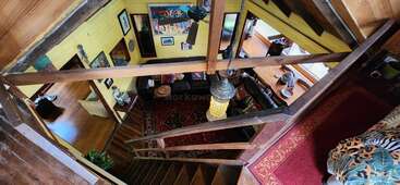 Das Bild zeigt das Innere eines Hauses aus einem hohen Winkel und zeigt eine Treppe, Holzbalken und ein Wohnzimmer mit einem roten Teppich und verschiedenen Möbeln.