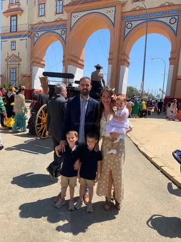 L'image représente une famille de quatre personnes posant pour une photo devant un grand bâtiment à arcades, entourée de personnes portant des vêtements traditionnels espagnols.