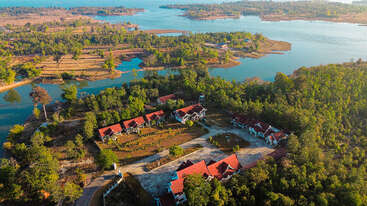 Essa imagem mostra uma paisagem pitoresca à beira do lago, com vegetação exuberante, casas com telhados vermelhos, caminhos sinuosos e corpos d'água tranquilos, criando um ambiente pacífico e cênico.