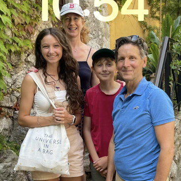 Vier Leute stehen draußen und lächeln für das Foto. Hinter ihnen sieht man Grünpflanzen und Steine. Eine Person hält eine Tragetasche in der Hand, auf der „THE UNIVERSE IN A BAG“ steht.