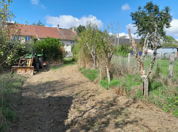 Scène rurale ensoleillée avec un tracteur, de l'herbe coupée, des arbres taillés, une ferme au toit rouge, un ciel bleu et de la verdure en arrière-plan.