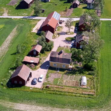 The image depicts an aerial view of a rural landscape featuring a cluster of red barns and houses amidst lush green fields and trees, with a road running through the scene.