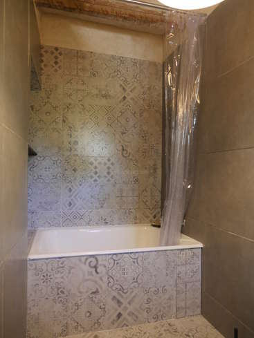 The image depicts a bathroom with a white bathtub, patterned tiles, and a clear shower curtain, featuring a light fixture above the tub.