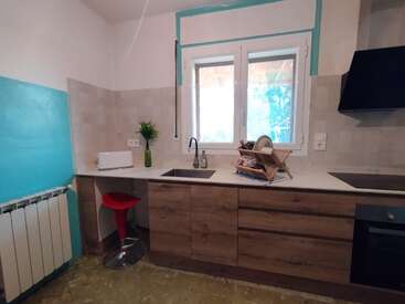 Diese moderne Küche hat Holzschränke, eine weiße Arbeitsplatte, ein Fenster, einen Geschirrkorb, einen roten Hocker, einen Toaster, eine grüne Vase, einen Elektroherd und geflieste Wände. Hell, ordentlich, praktisch.